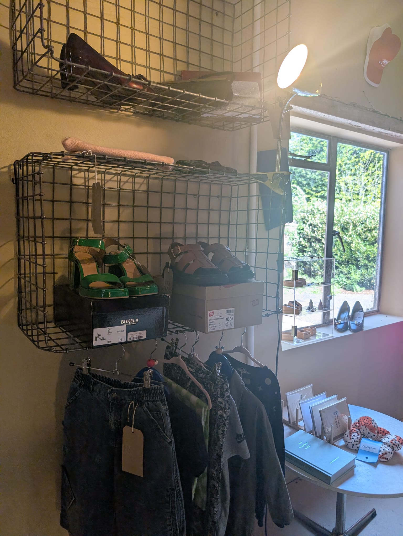 Wire baskets holding green sandals, denim hanging below, and an open window onto the garden